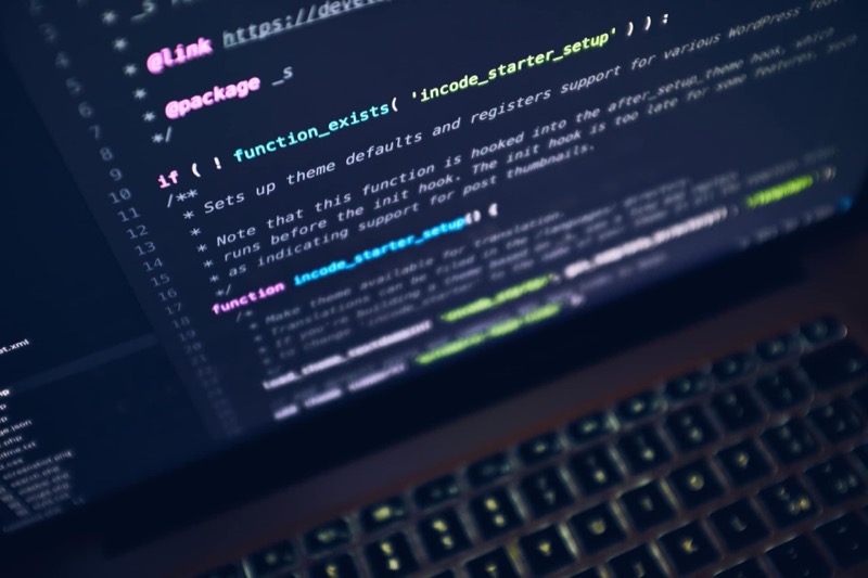 Computerbildschirm zeigt bunten Quellcode und eine beleuchtete Tastatur im Vordergrund.